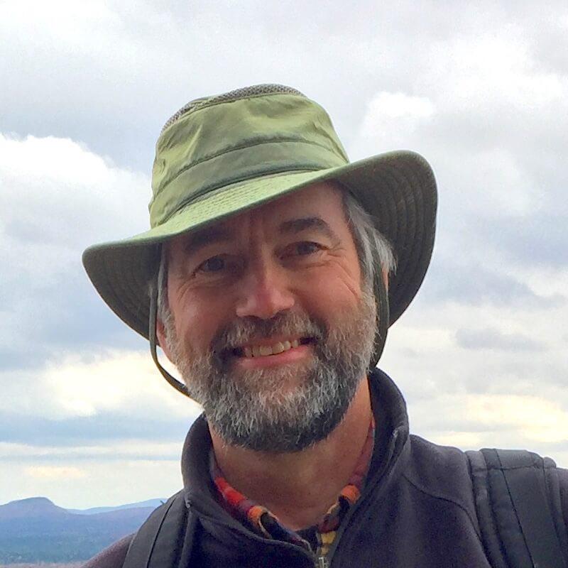 Walt in a green hat smiling against a cloudy sky