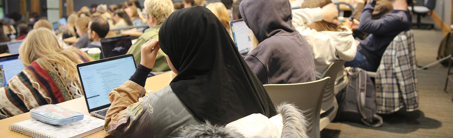  A crowd of students in a lecture hall, focused on the speaker at the front of the room.