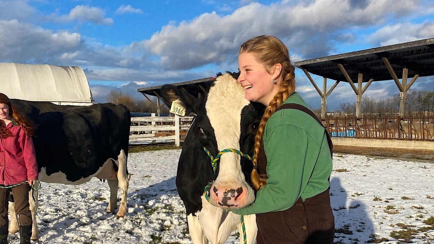 Annie Boudrea smiling with a Holstein cow outdoors at the UVM Dairy Barn 