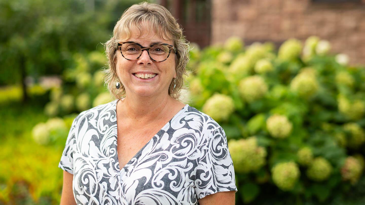 corinne thompson smiles while standing outside in front of flowers