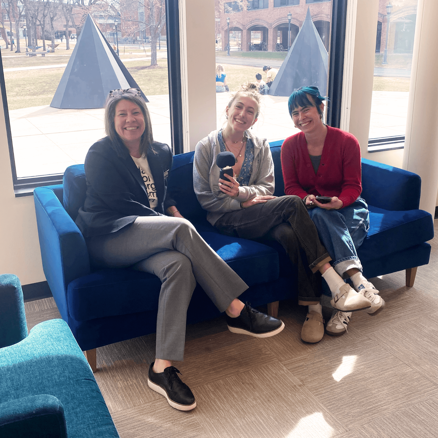 Three women sit on a blue couch in front of windows in the Fleming's lobby.