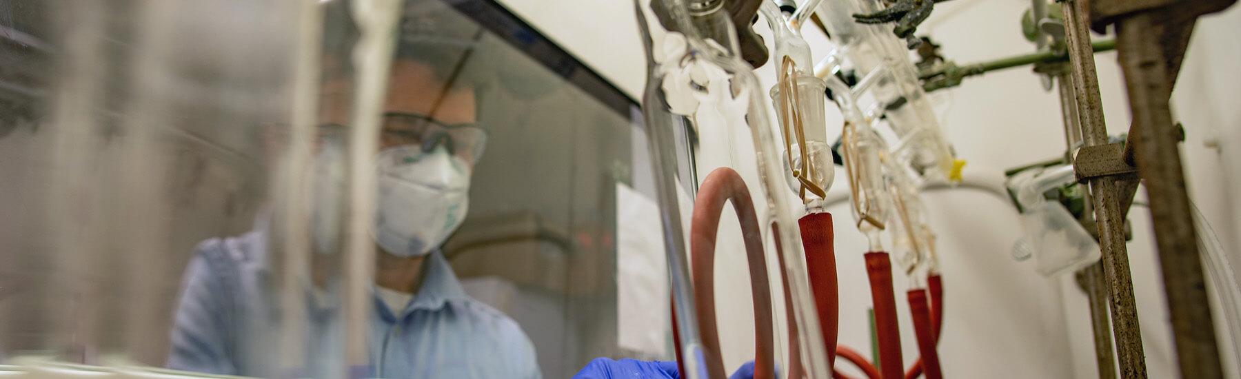 A man with a mask in a chemistry lab working near fume hood