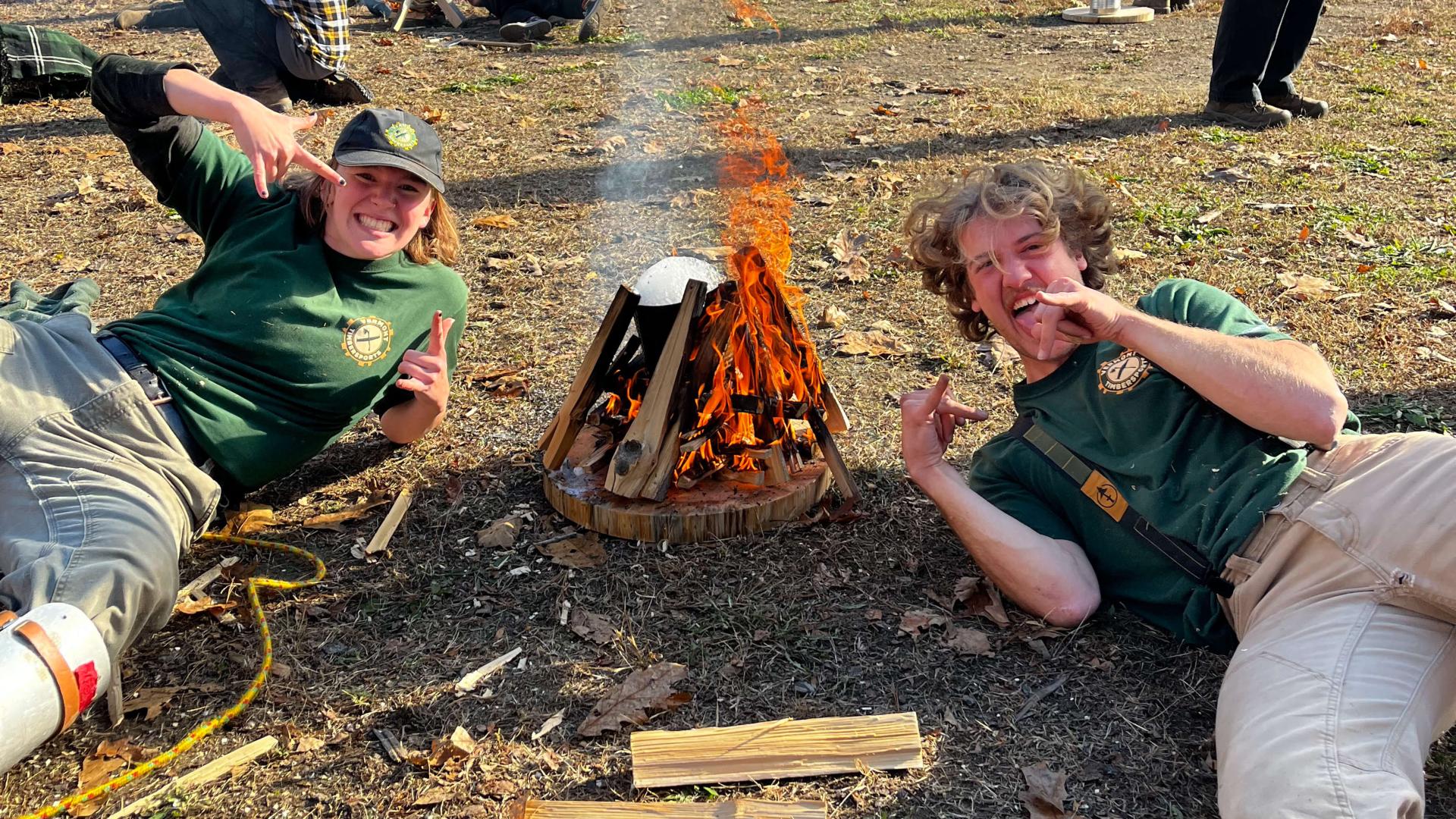 Es and a friend posing next to a campfire they built.