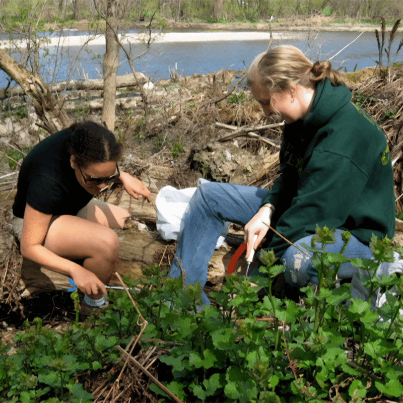 Two students are shown doing work on a river bank