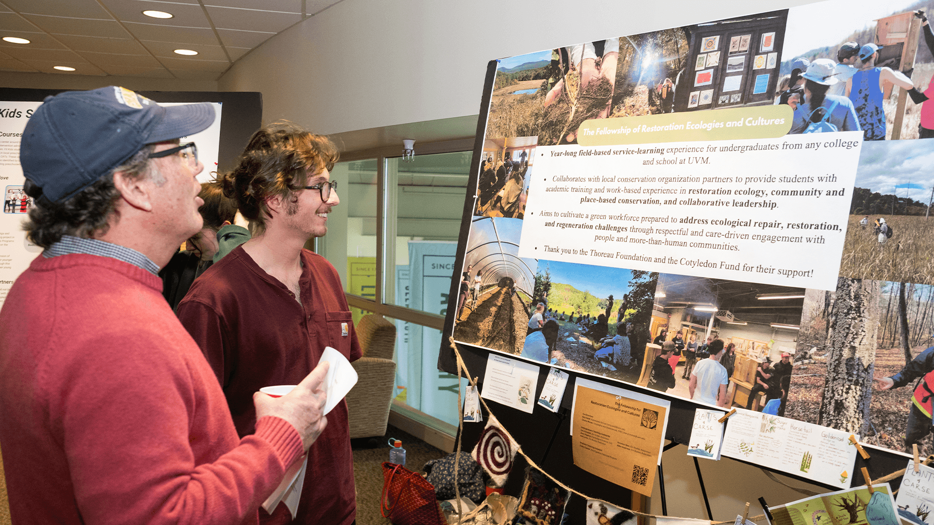 Two people view a colorful student poster display about restoration ecology at a showcase event.