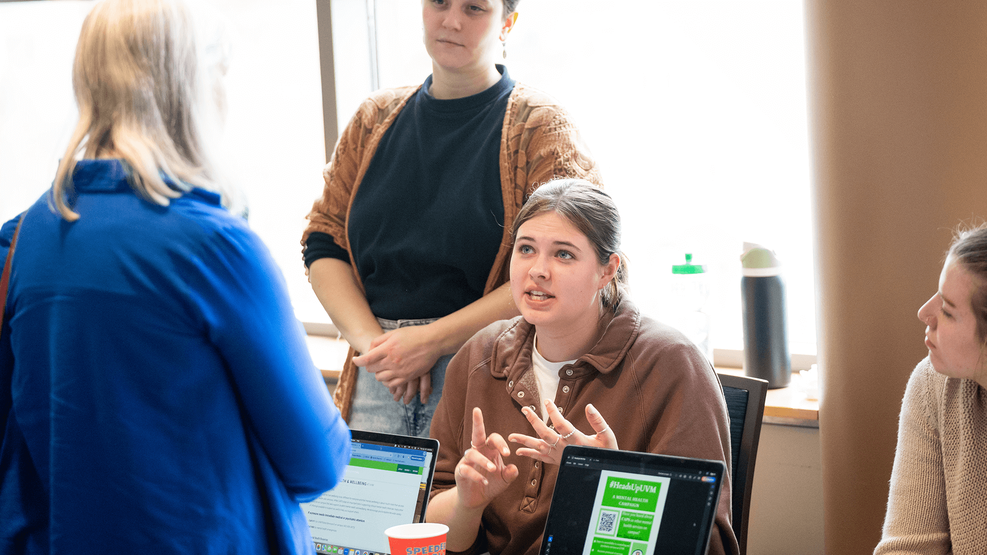 Student explains a slideshow presentation to an attendee during an indoor showcase event.
