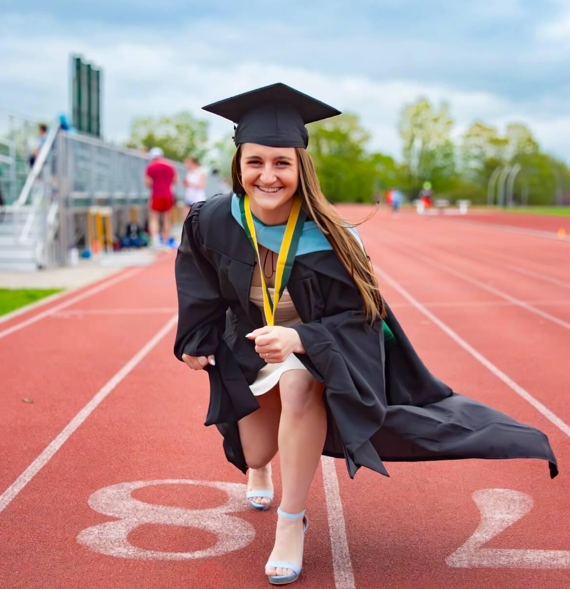 Maggie Sorrentino dressed in regalia positioned as sprinter on the outdoor UVM track