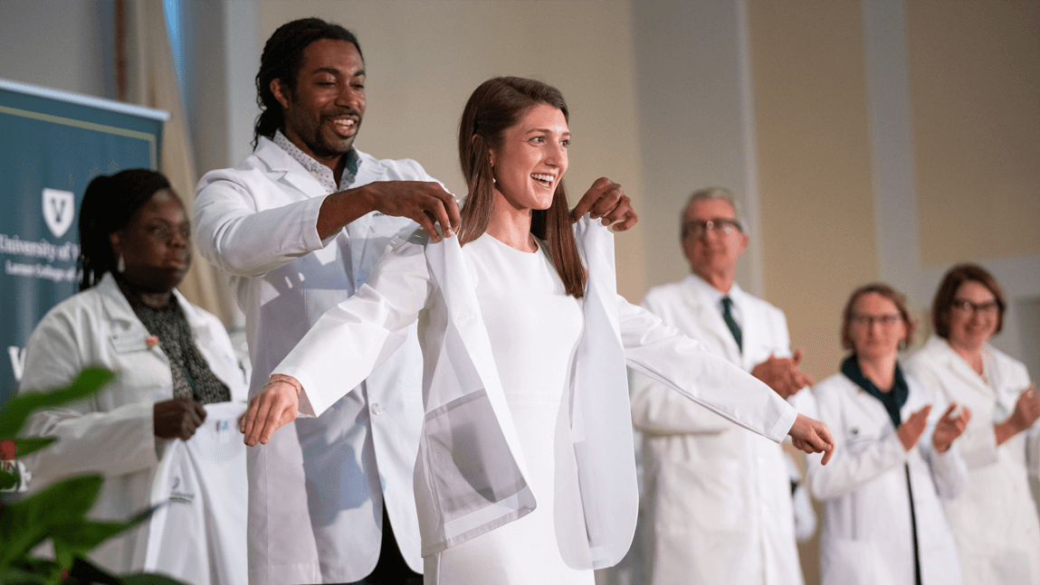 Class of 2028 medical student Caroline Donohue receives her white coat on the stage in UVM's Ira Allen Chapel from Tony Williams, M.D., assistant professor of family medicine and assistant dean of admissions.
