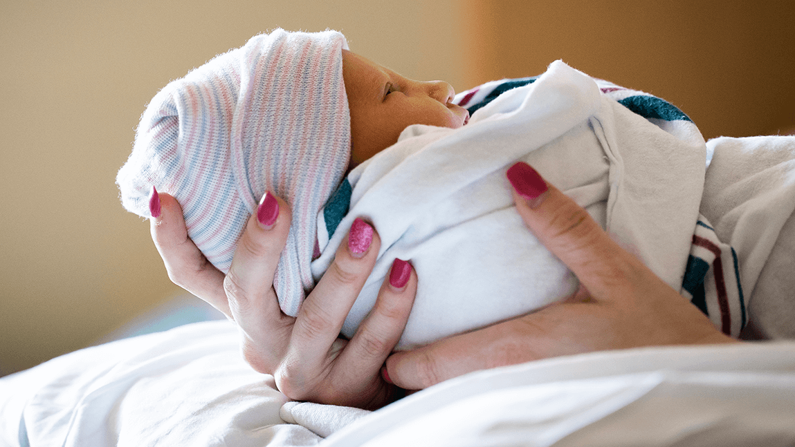 a swaddled newborn baby being held