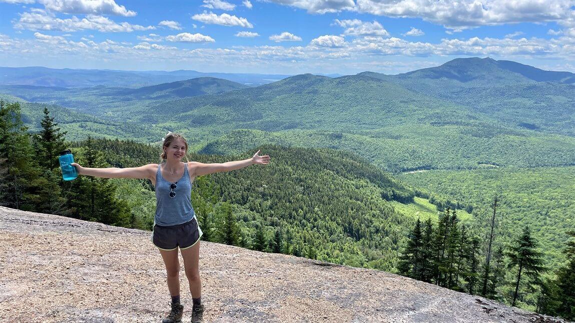Deniz Dutton standing on a hiking trail with a green mountainous view behind her
