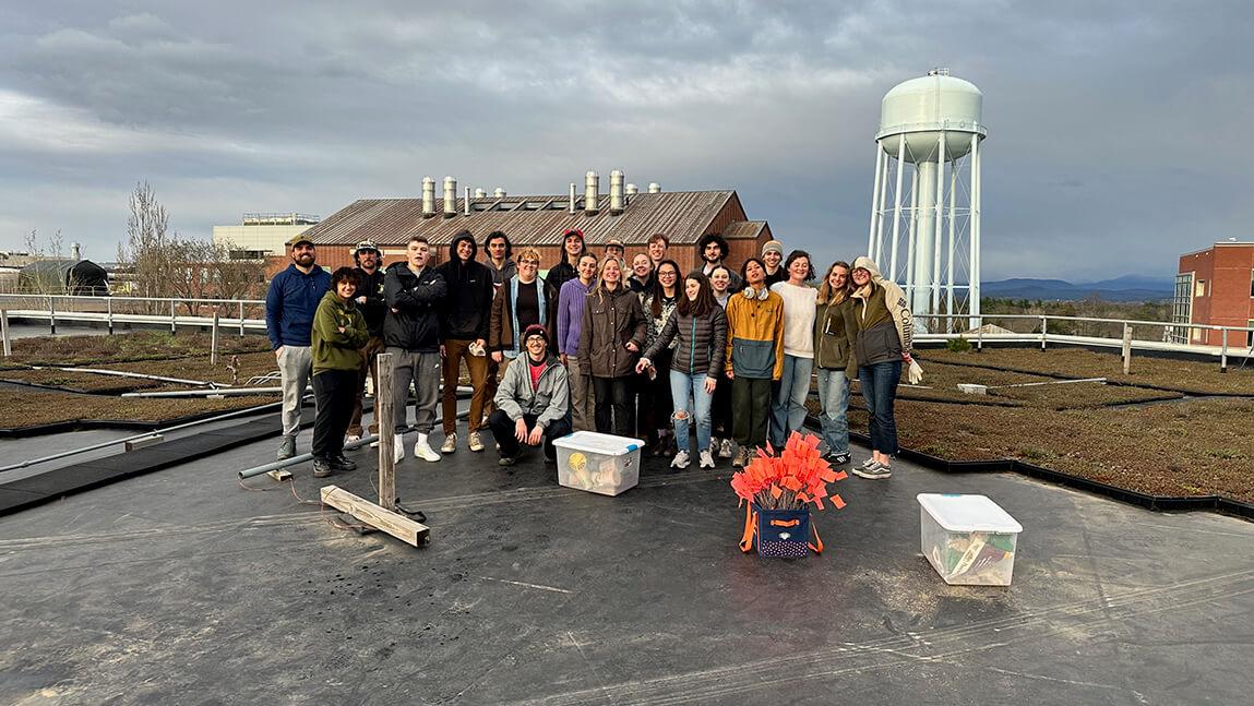 Group of 20 students stand on top of green roof overlooking view of University of Vermont campus.