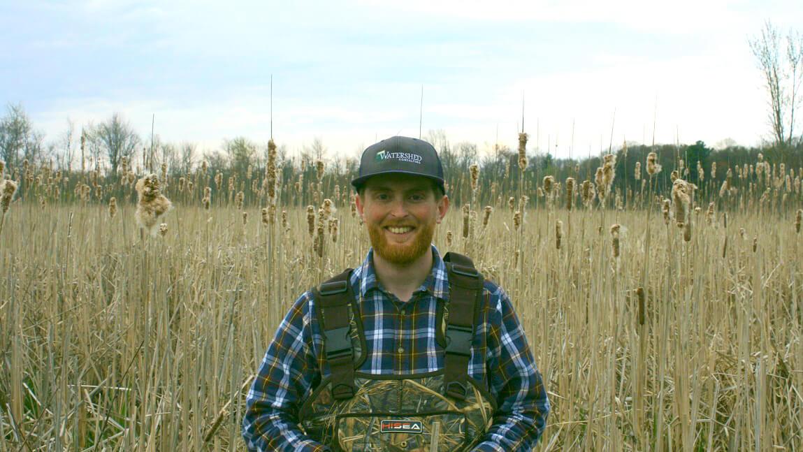 Sam Buswell standing among reeds in a wetland in Vermont