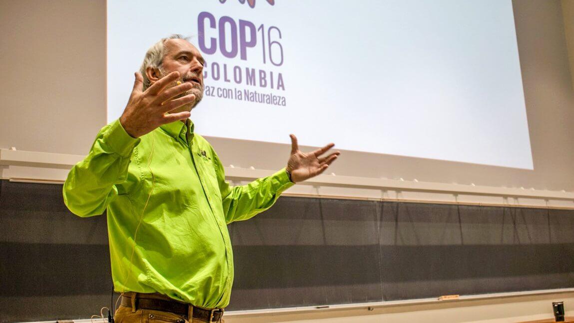 Walter Poleman giving a lecture at the front of a classroom with the COP16 logo on the screen behind his head