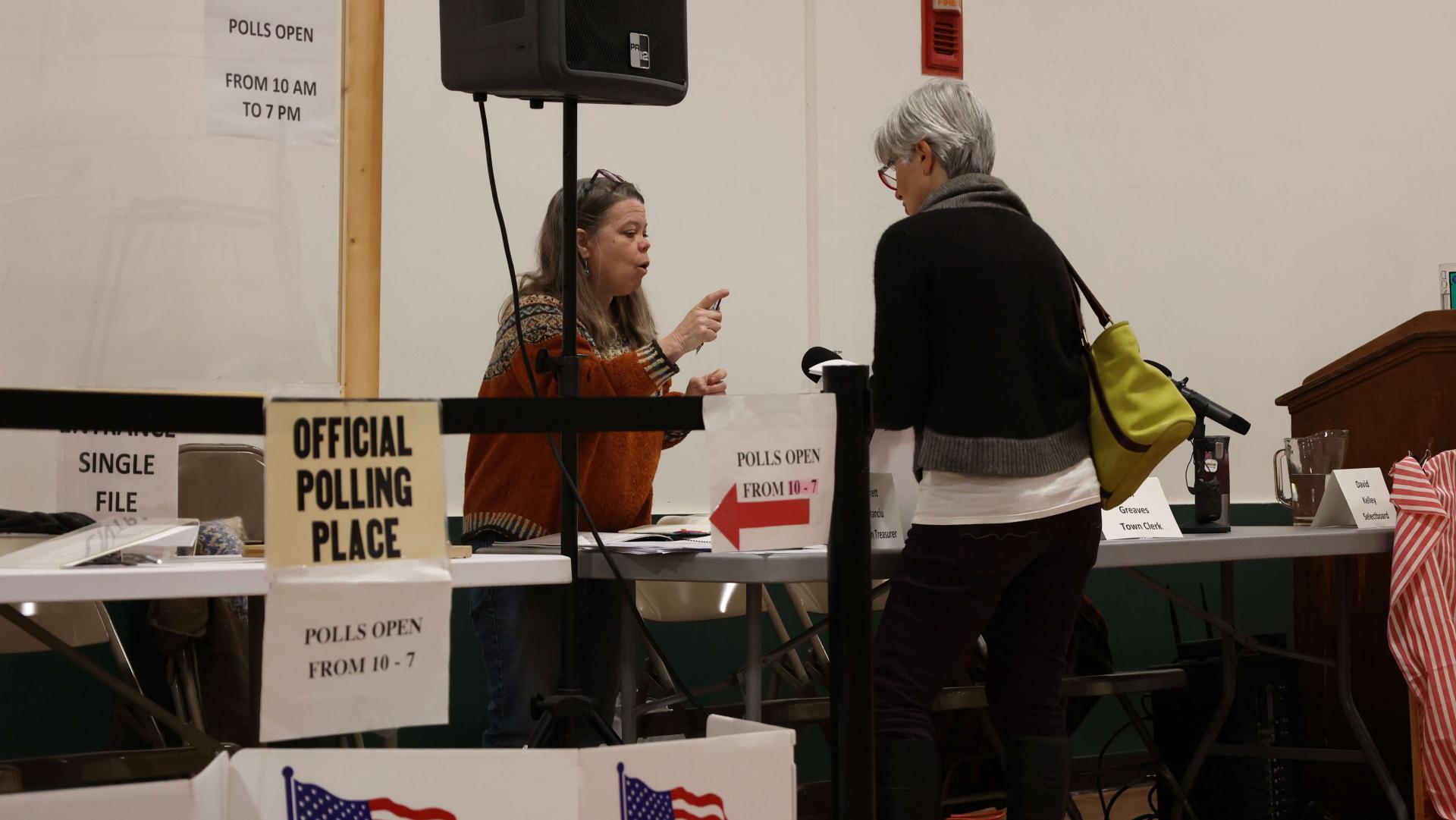 female poll worker chats with voter at a polling place surrounded by election-related signs