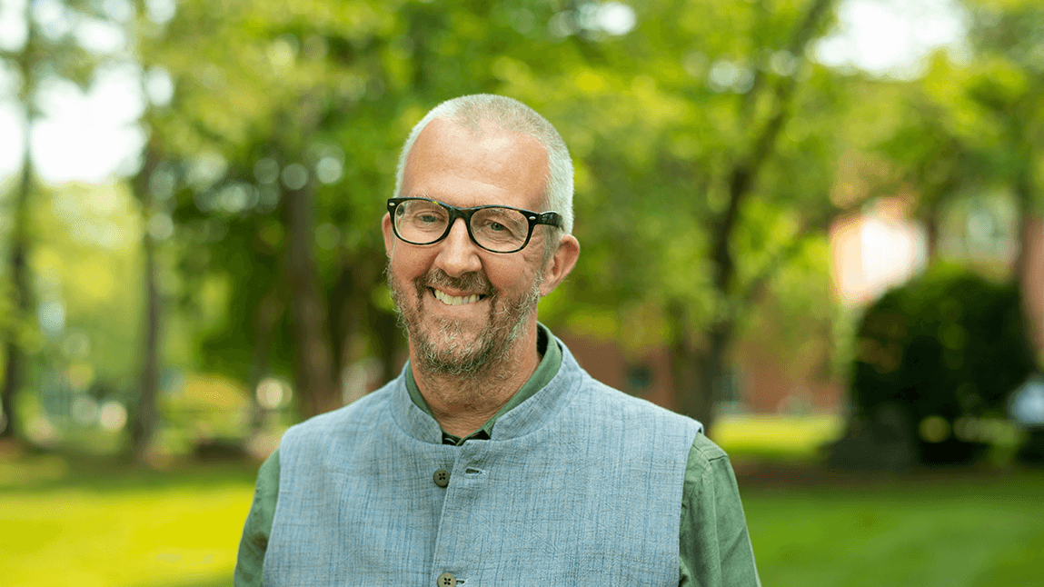 Mark Usher, smiling on a sunny day with green trees and bushes in the background