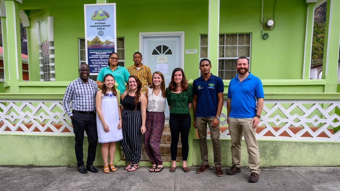 group of students, faculty and partners standing in front of a green building that has a sign reading "PItons Management Area"