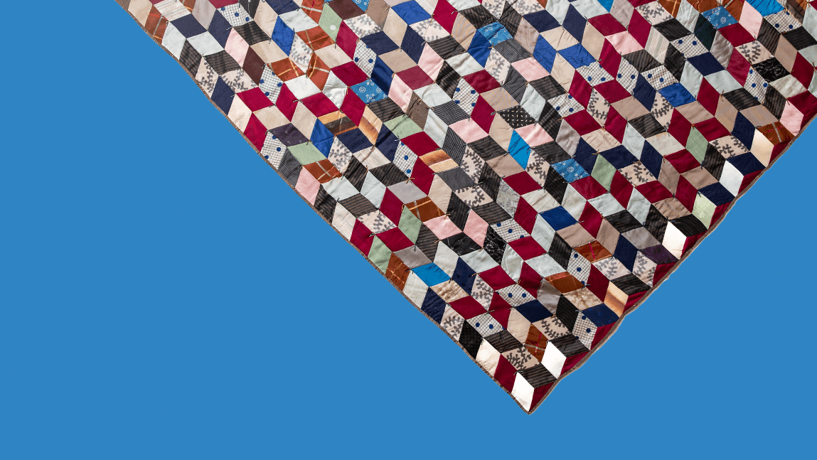 A corner of a multi-color quilt dips diagonally down over a field of bright sky blue.