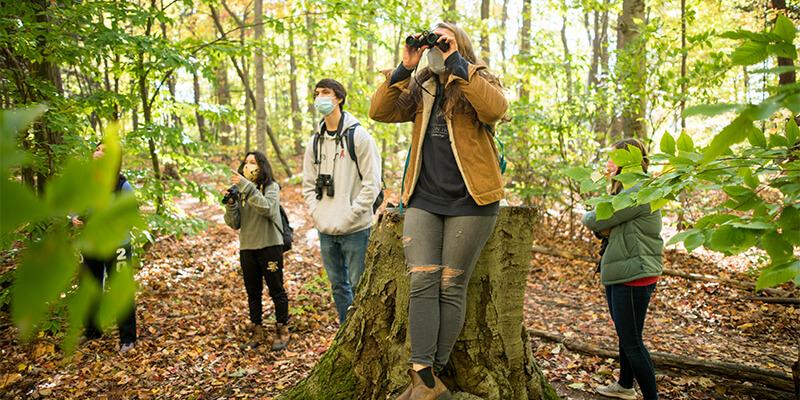 Four college students with face masks and binoculars in the woods