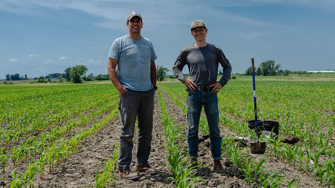 Joshua Faulkner and Ben Tutko stand with shovels in a corn field