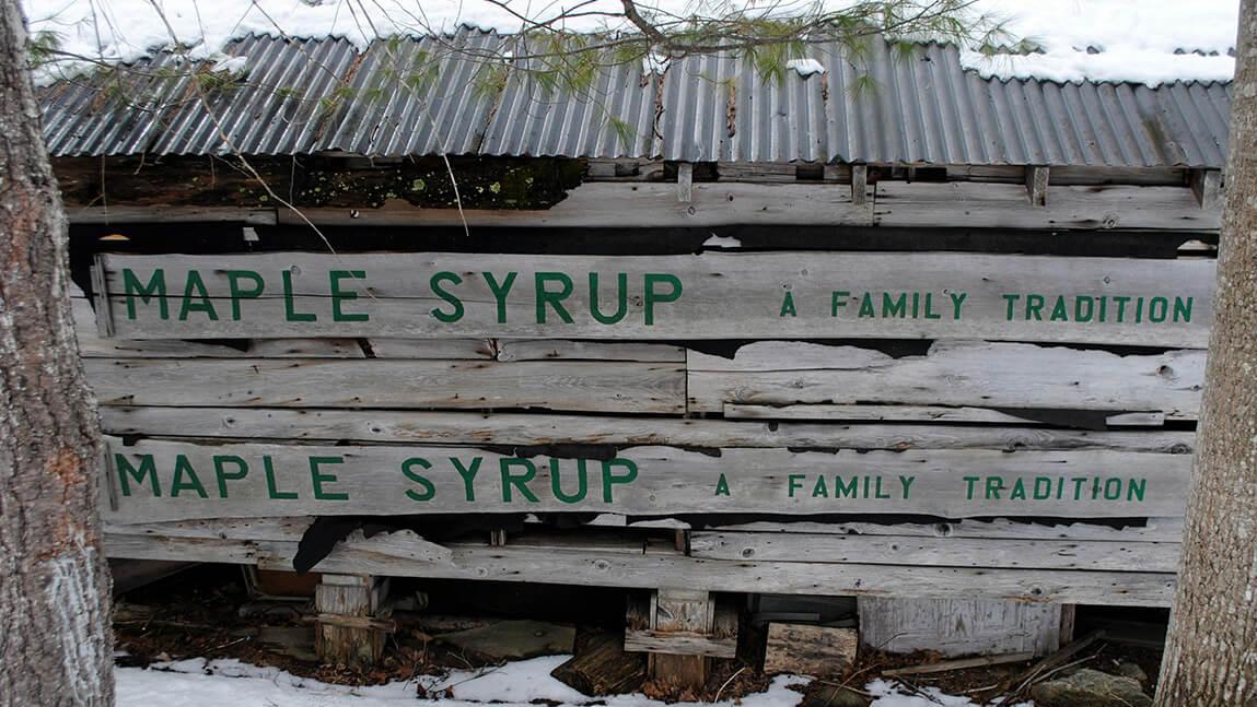 dilapidated shack with words painted on it: maple syrup a family tradition
