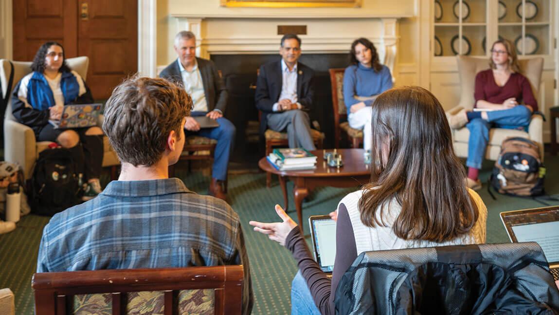two students with their back to the camera have a discussion while a group people around them listens