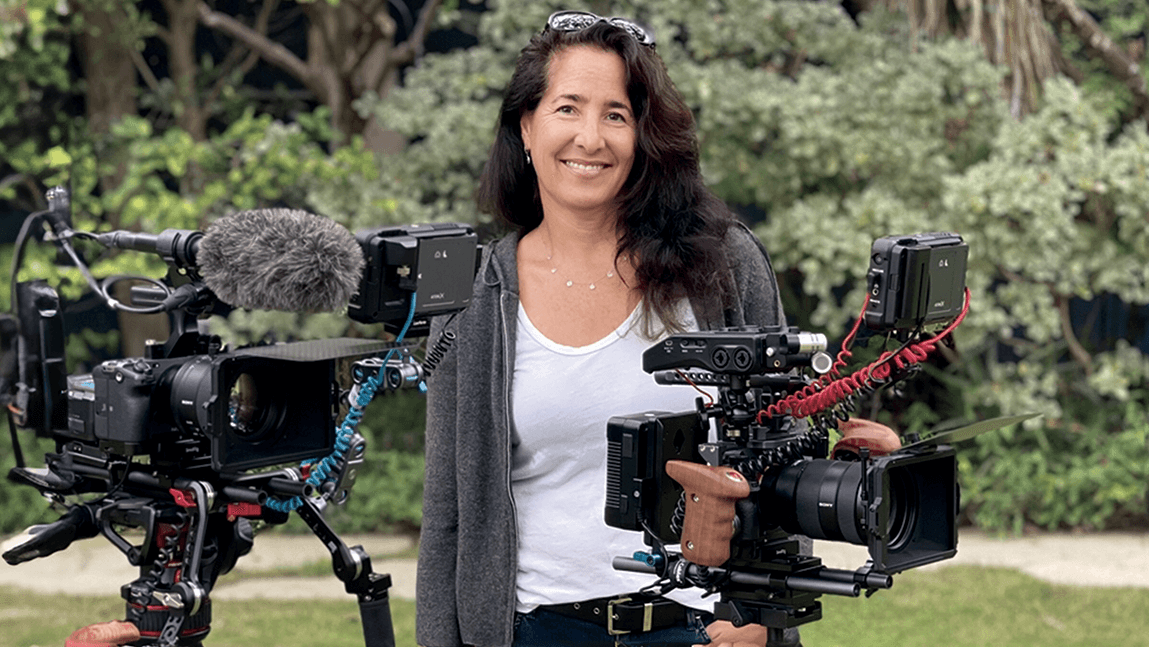 a woman holding a video camera in front of a line of trees