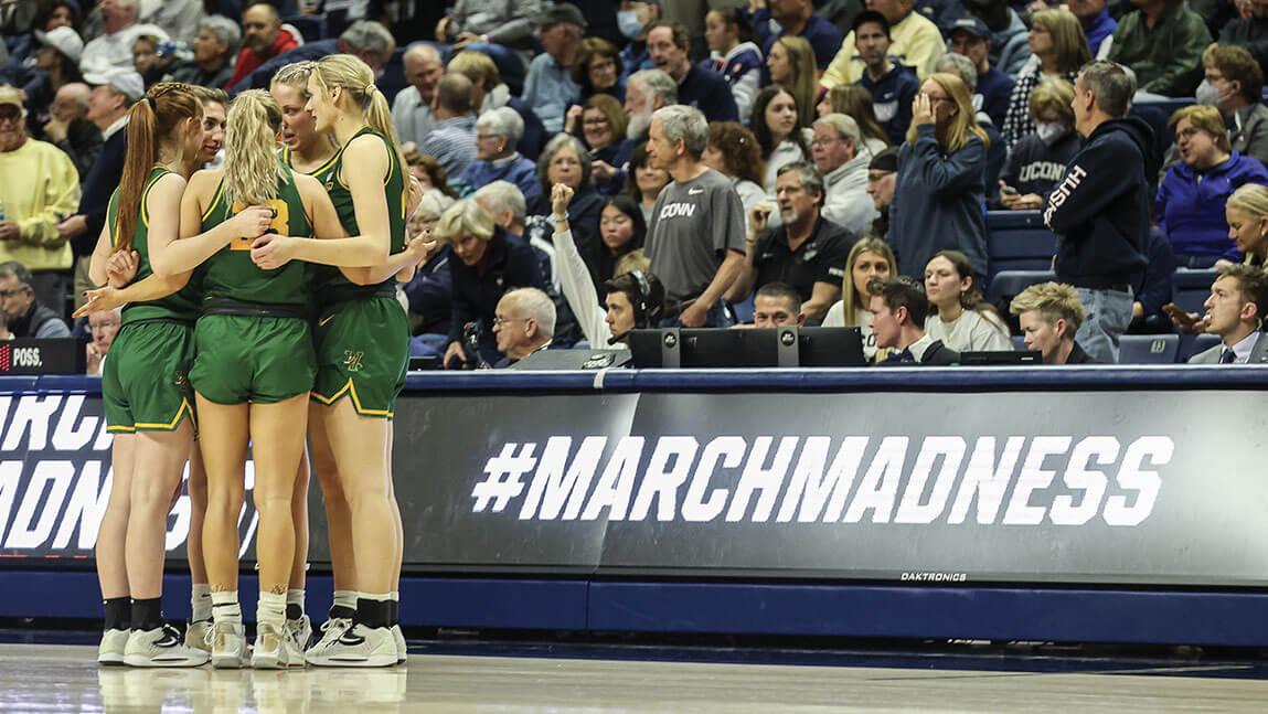 A group of UVM women's basketball players huddles on the court